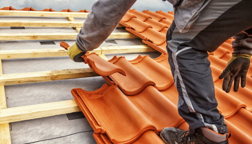 Mężczyzna układa dachówkę na wytrzymałej drewnianej konstrukcji dachowej