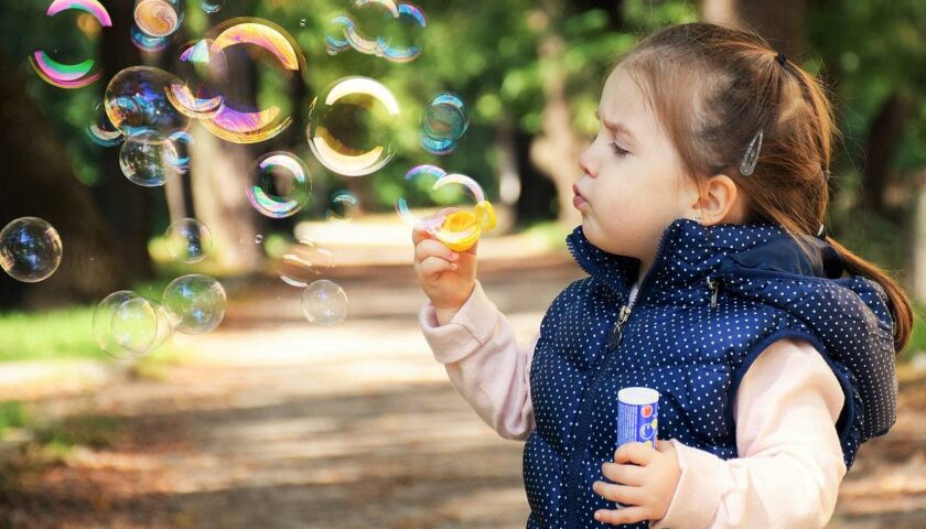 Dziewczynka puszcza banki mydlane będąc na spacerze w parku z rodzicami